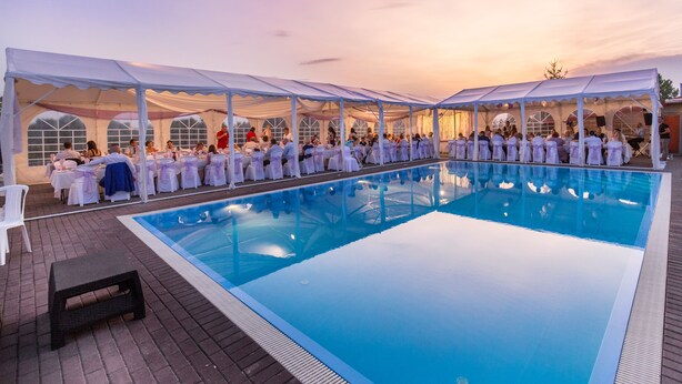 A poolside event with a covered area and tables, surrounded by a pool.