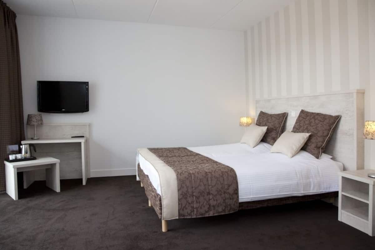 Una habitación de hotel con cama, escritorio, televisión y lámparas de noche.