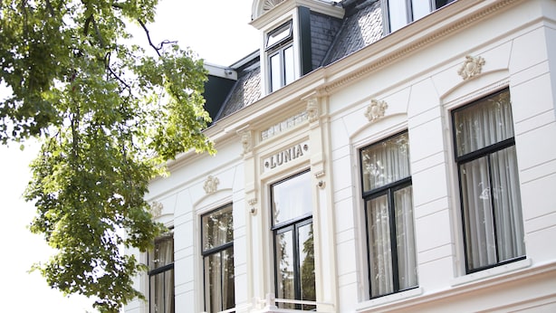 Un bâtiment blanc dont la façade porte l’inscription « LUNIA », avec de grandes fenêtres et un balcon agrémenté d’une balustrade.