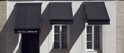 A hotel facade with three windows and a black awning with the text "HOTEL MONTRAND".