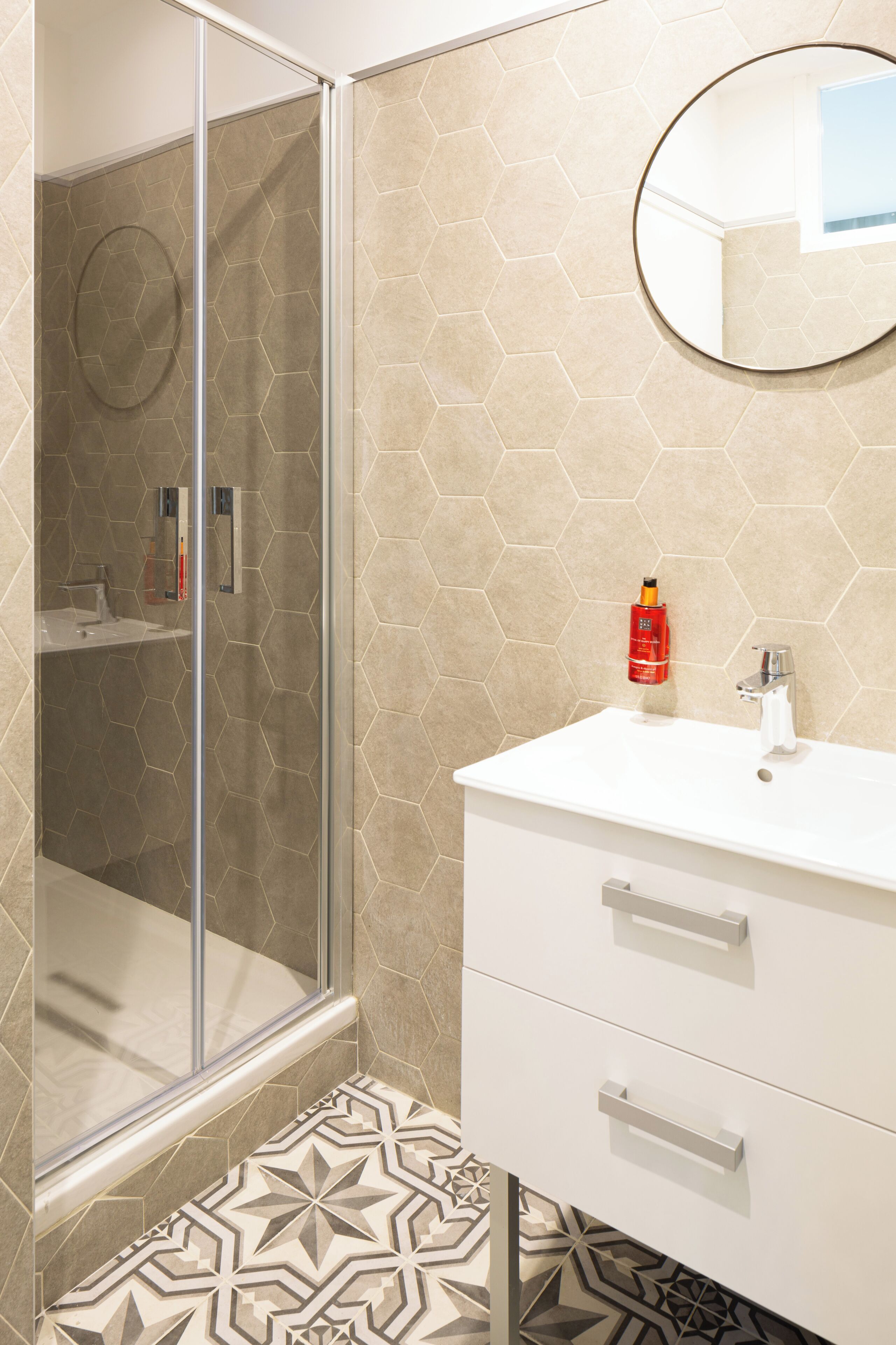 A bathroom with a glass shower enclosure, a white sink, and a round mirror on the wall.
