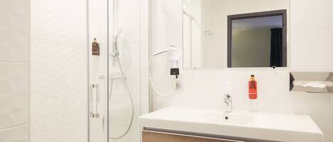 A modern bathroom with a glass shower enclosure, a white sink with wooden cabinet drawers, and a mirror above the sink.