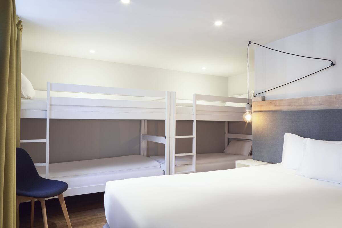 Une chambre avec un lit superposé, un bureau et une chaise, une table de chevet et une lampe fixée au mur.