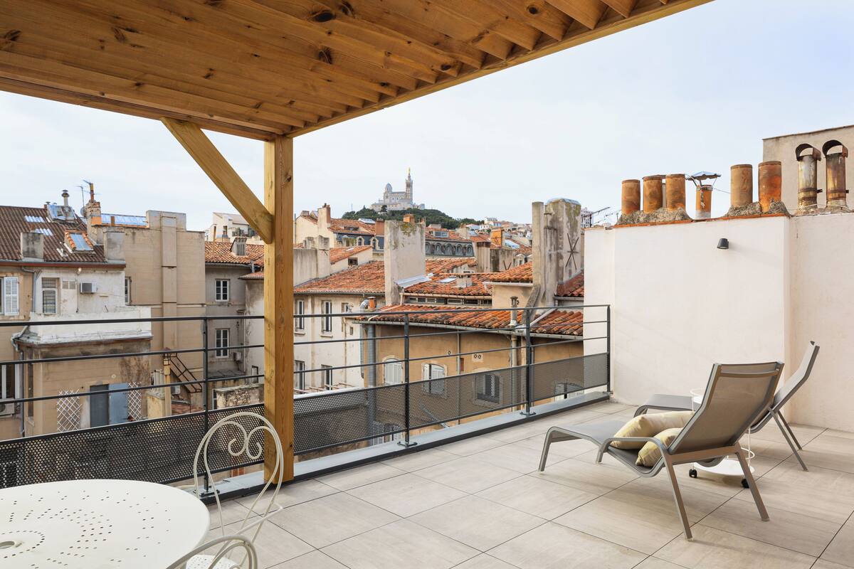 Un balcon avec une table et deux chaises, offrant une vue sur le paysage urbain, avec ses bâtiments historiques et son imposante tour.
