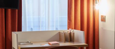 A hotel room with a desk, a chair, a TV, and curtains.