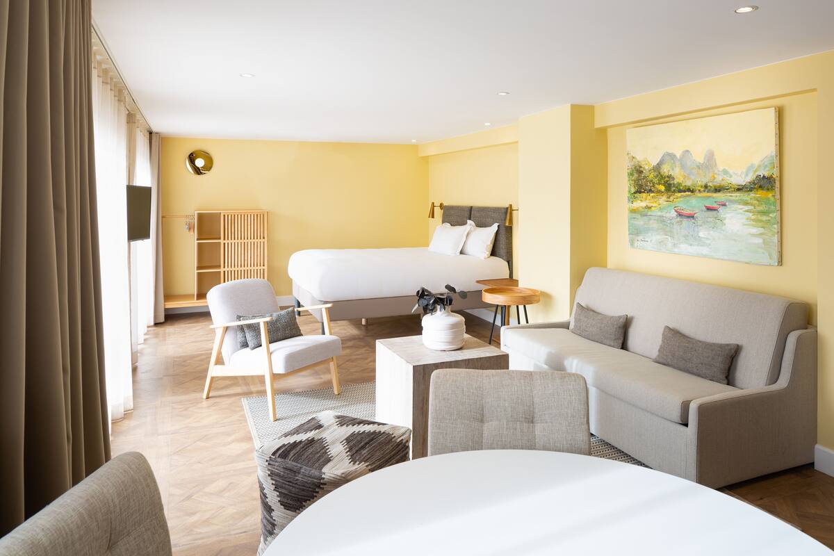 Une chambre d’hôtel avec un lit, un canapé, une chaise, une petite table et un tableau au mur.