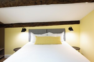 A bed with white linens, a yellow pillow, and a headboard with a grey panel. There are two bedside tables with lamps.