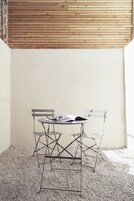 A corner with a small table and two chairs, a wooden slatted ceiling, and a plain wall.