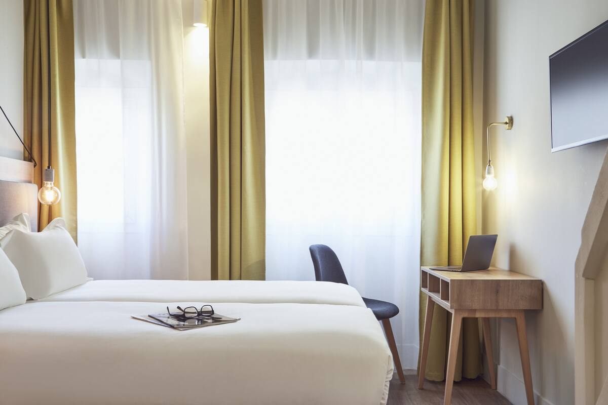 Une chambre d’hôtel équipée d’un lit, d’un bureau, d’une chaise et d’un téléviseur fixé au mur.
