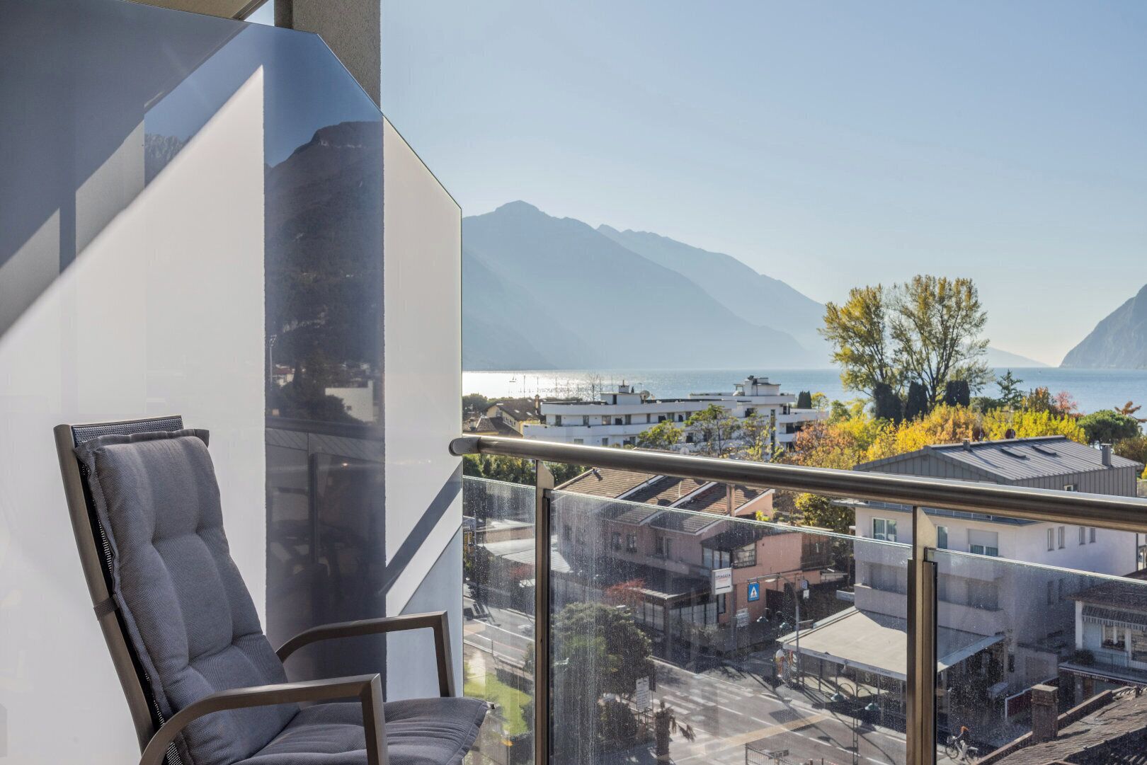 A modern balcony with a glass railing overlooking a cityscape and mountains.