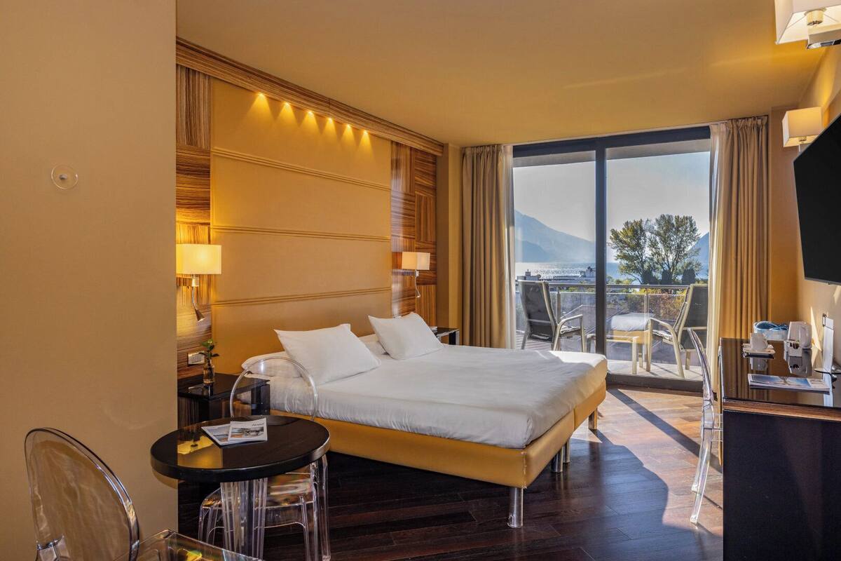 Une chambre d’hôtel avec un grand lit, un bureau avec une chaise, une petite table et une vue sur l’extérieur.