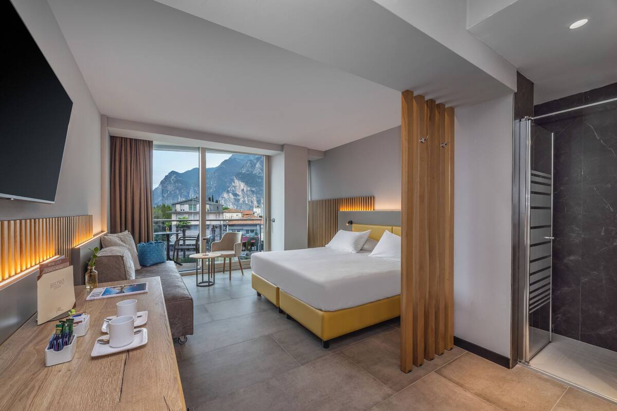 Une chambre d’hôtel moderne dotée d’un grand lit, d’une tête de lit en bois, d’un bureau avec un coin café et offrant une vue sur les montagnes grâce à de grandes fenêtres.