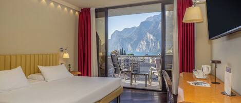 A hotel room with a bed, a desk, a chair, a TV, and a balcony with a mountain view.