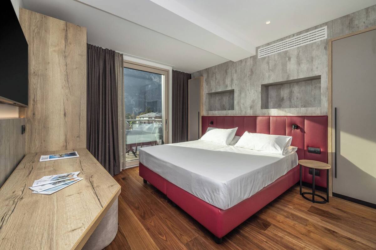 Une chambre d’hôtel moderne avec un grand lit, un bureau en bois et une vue sur un balcon.