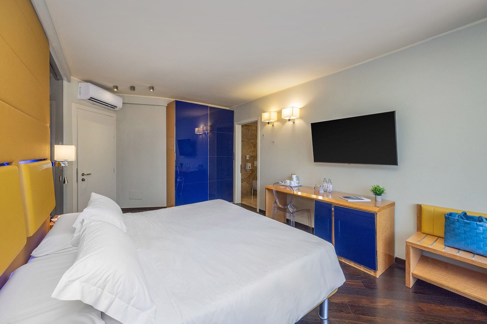 A hotel room with a bed, a desk, a TV, and a seating area.