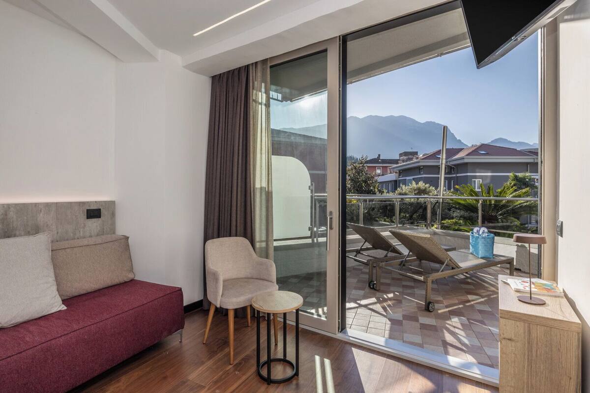 Une chambre moderne équipée d’un canapé, d’un fauteuil, d’une télévision et d’un balcon offrant une vue sur les bâtiments et les montagnes.