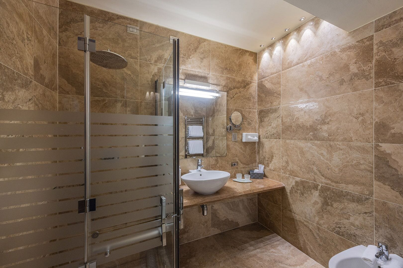 A modern bathroom with a glass shower enclosure, a large sink, and a bidet.