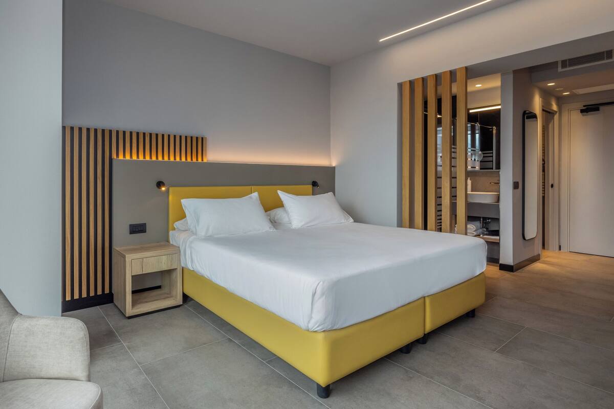 Une chambre à coucher moderne avec un lit jaune, une literie blanche, une table de chevet en bois et une tête de lit intégrée.