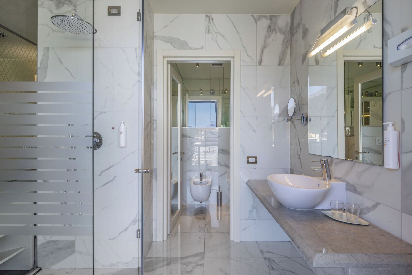 Un baño moderno con ducha de vidrio, un lavamanos grande con encimera de mármol y un espejo sobre el lavamanos.