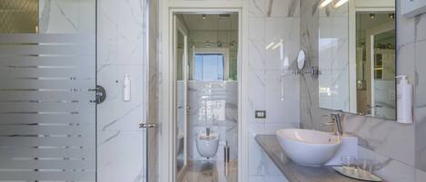 Une salle de bain moderne avec une douche à parois de verre, un grand lavabo doté d’un plan de travail en marbre et un miroir au-dessus du lavabo.