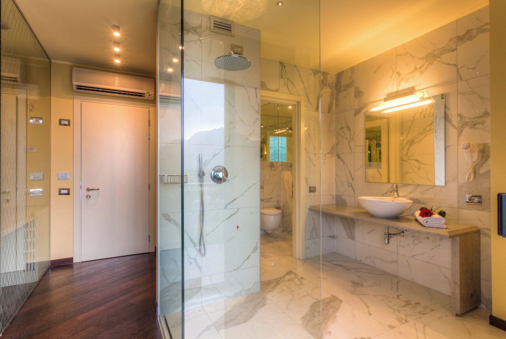 Une salle de bain moderne avec une douche à parois de verre, un sol carrelé en marbre et un grand miroir au-dessus du lavabo.