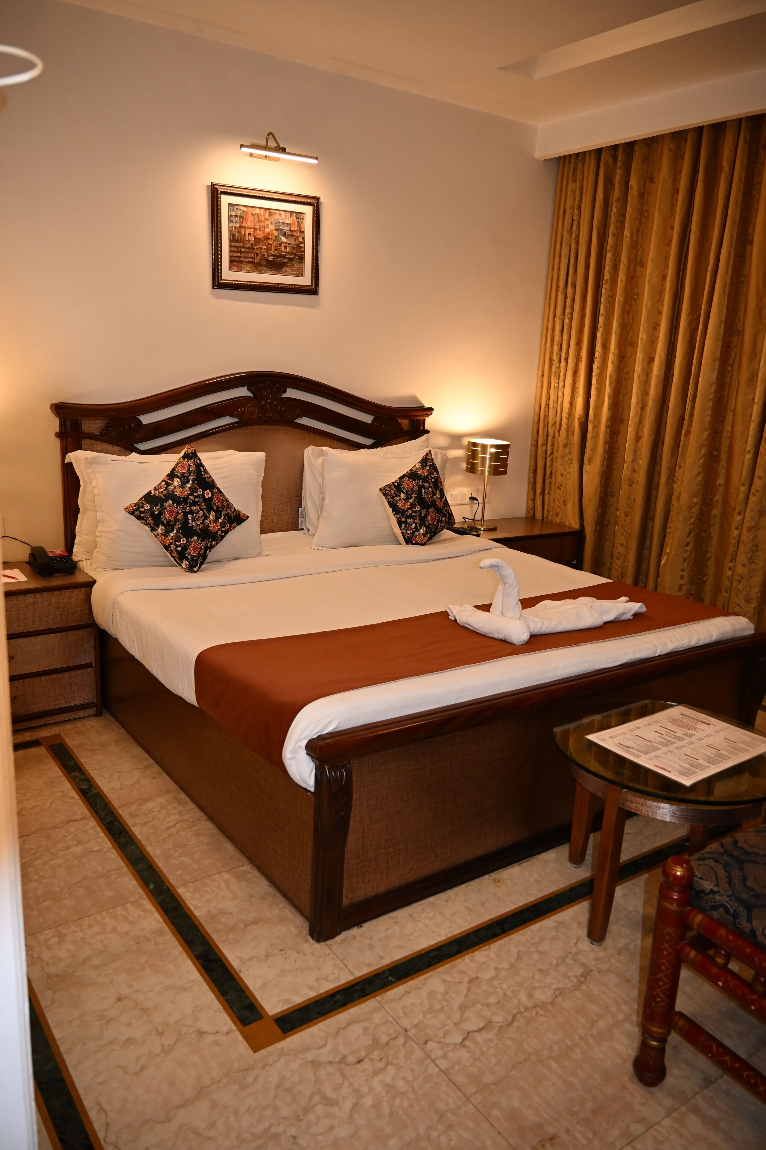 Habitación de hotel con una cama grande, una mesita de noche, una silla, una lámpara y un cuadro en la pared.