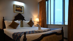 Une chambre d’hôtel avec un grand lit, une table de chevet, une lampe, une fenêtre avec des rideaux et un tableau encadré au mur.