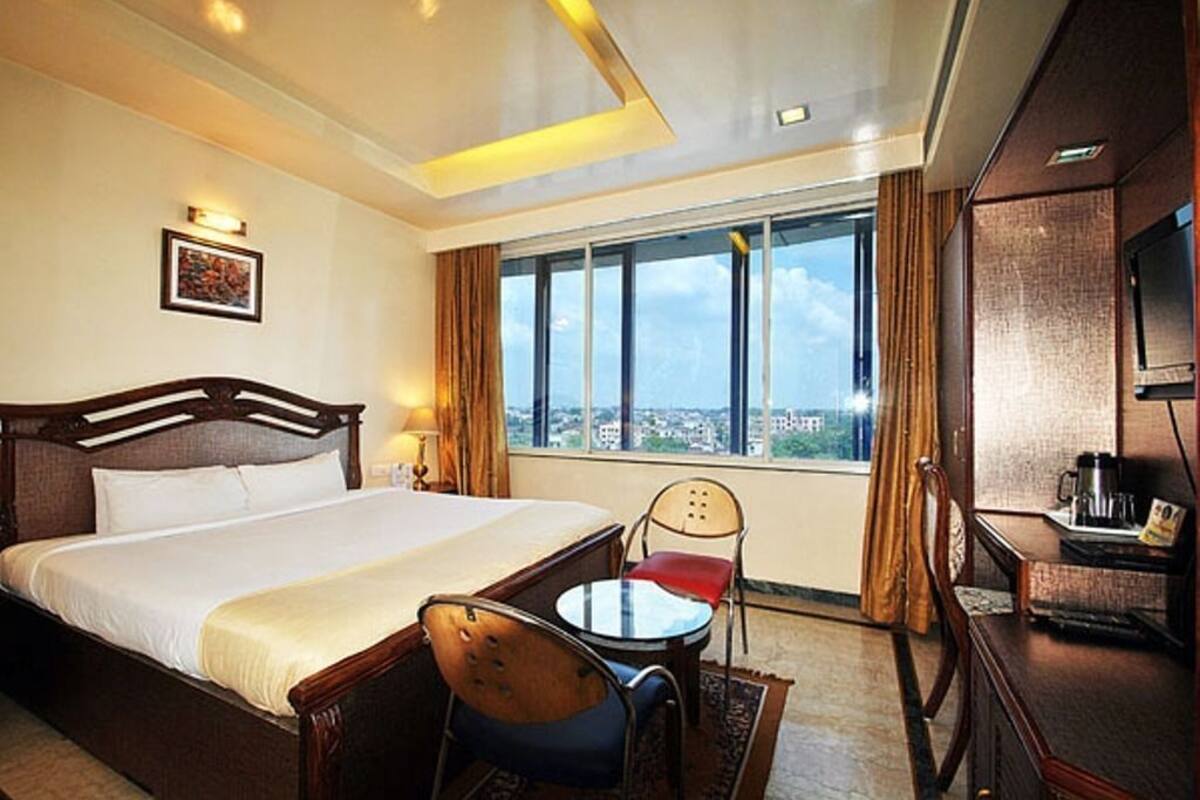 Habitación de hotel con una cama grande, una mesita, una silla, un televisor y una ventana con vista a la ciudad.
