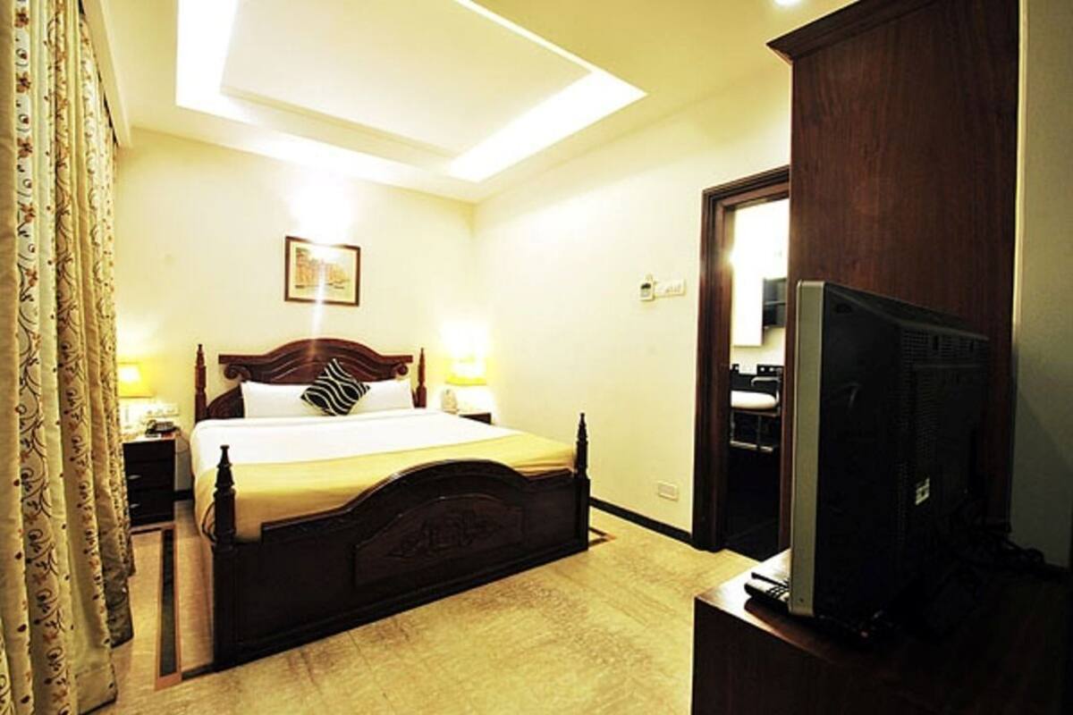 Una habitación de hotel con cama, lámparas de noche, televisor y armario de madera.
