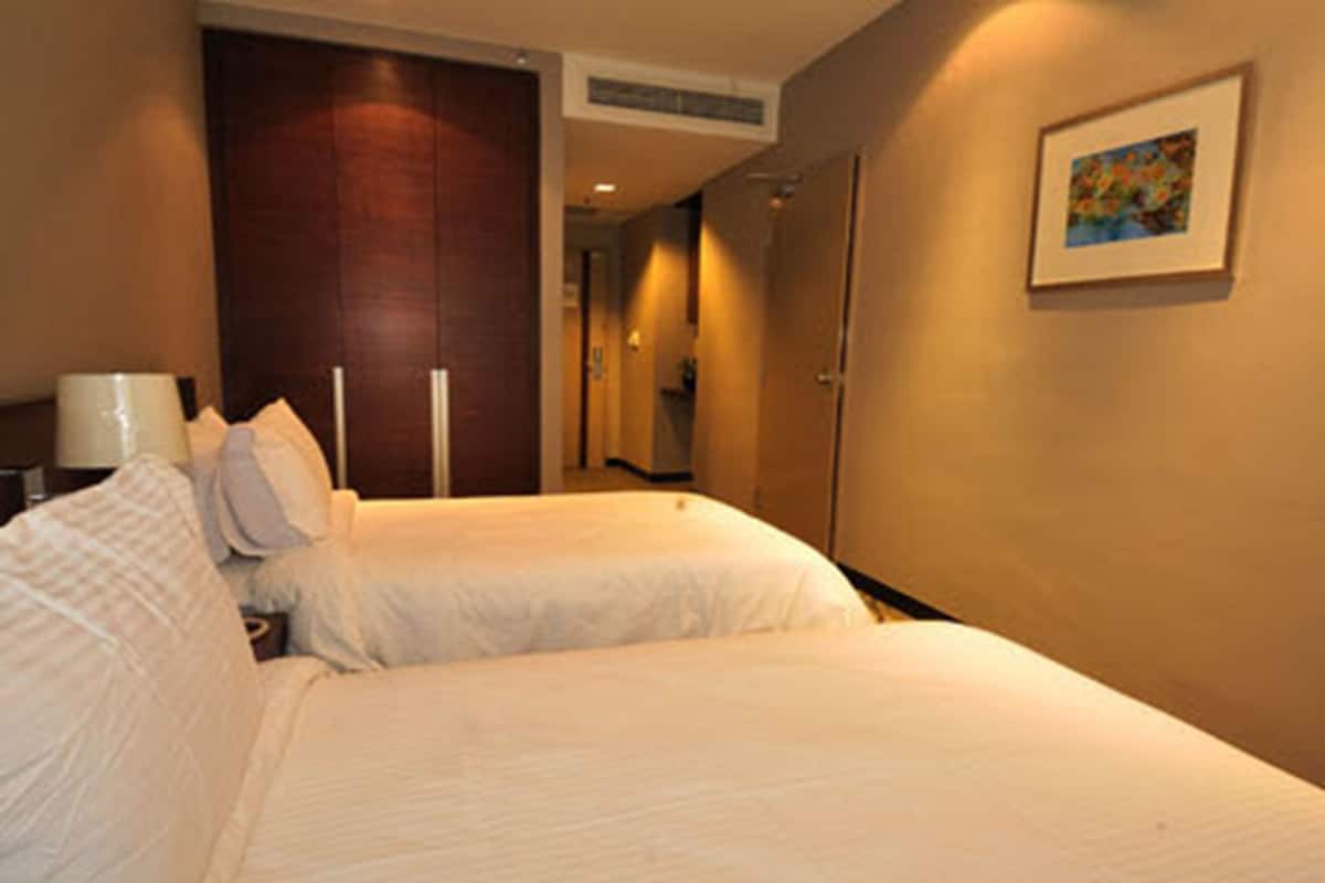 Une chambre d’hôtel avec deux lits, une table de chevet, une lampe, un tableau au mur et une porte donnant sur une autre pièce.