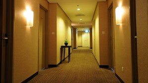 Un pasillo de hotel con pisos alfombrados, lámparas fijadas a la pared y una puerta al final.