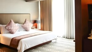 Habitación de hotel con una cama grande, dos almohadas, una mesita de noche con lámpara y una ventana con cortinas.