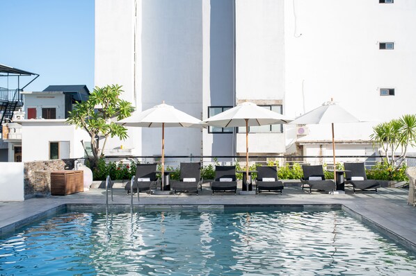 A pool area with lounge chairs and umbrellas, surrounded by a white building with a modern design.
