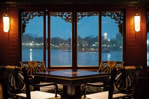 A dining area with a table and chairs, large windows with decorative frames, and wall-mounted lights. - Rosaleen Boutique Hotel (Hue)