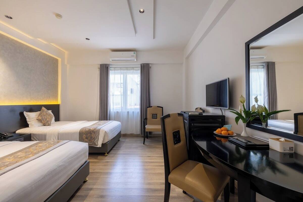 A hotel room with two beds, a desk, a chair, a TV, and a window with curtains.