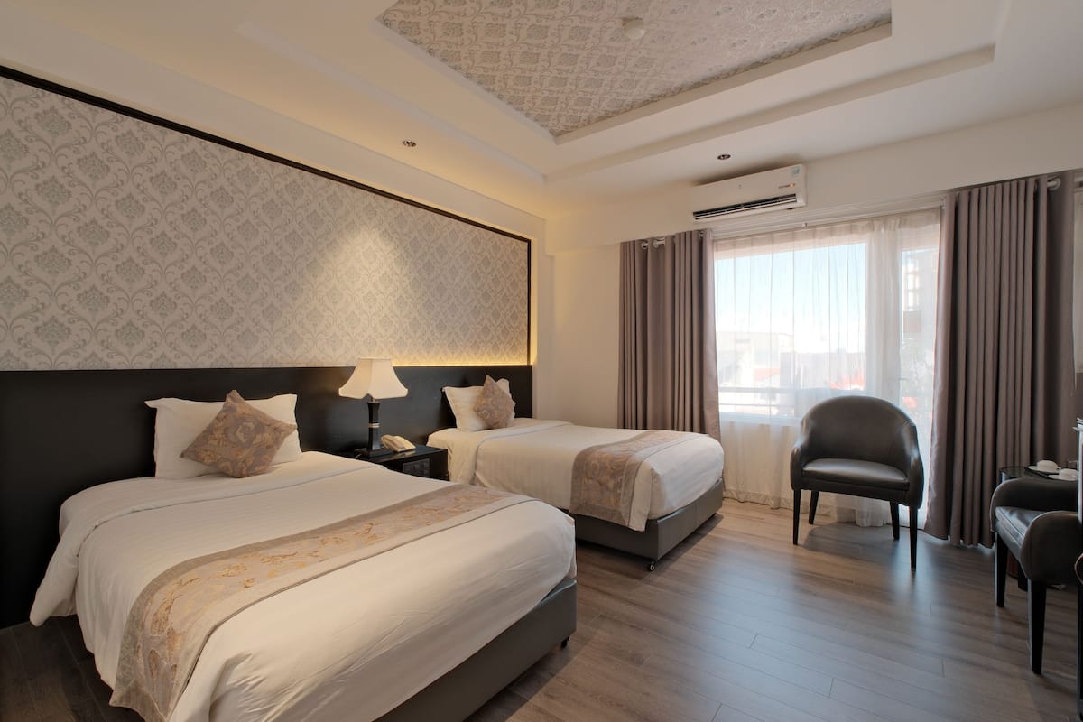 A hotel room with two beds, a desk, a chair, and an air conditioning unit.