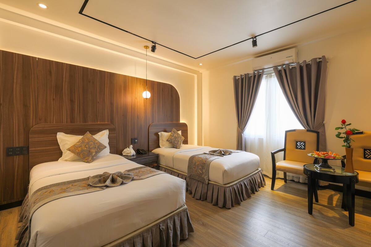 A hotel room with two beds, a sofa, a small table, and a window with curtains.