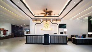 A modern hotel reception area with a central desk, a ceiling fan, and a large illuminated logo.