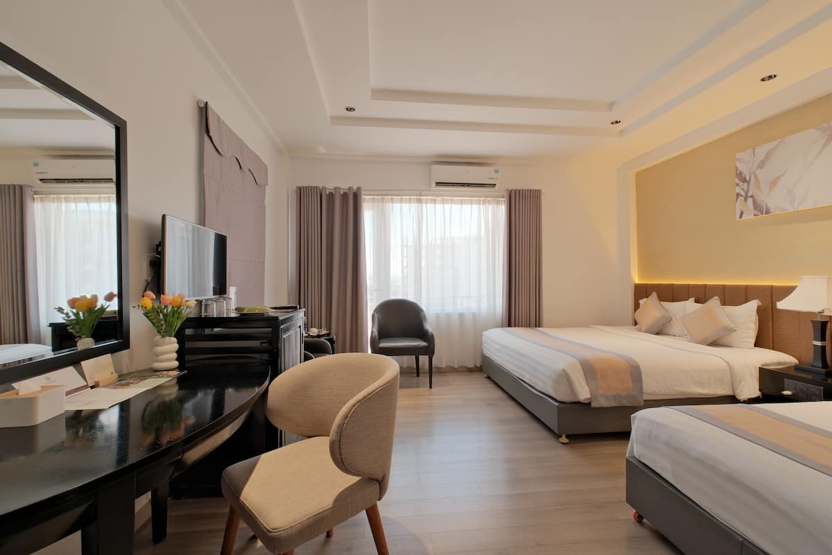 A hotel room with a desk, chair, two beds, a large mirror, and an air conditioning unit.