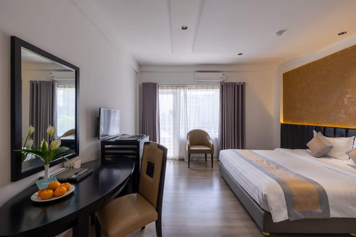 A hotel room with a bed, desk, chair, and a large mirror.