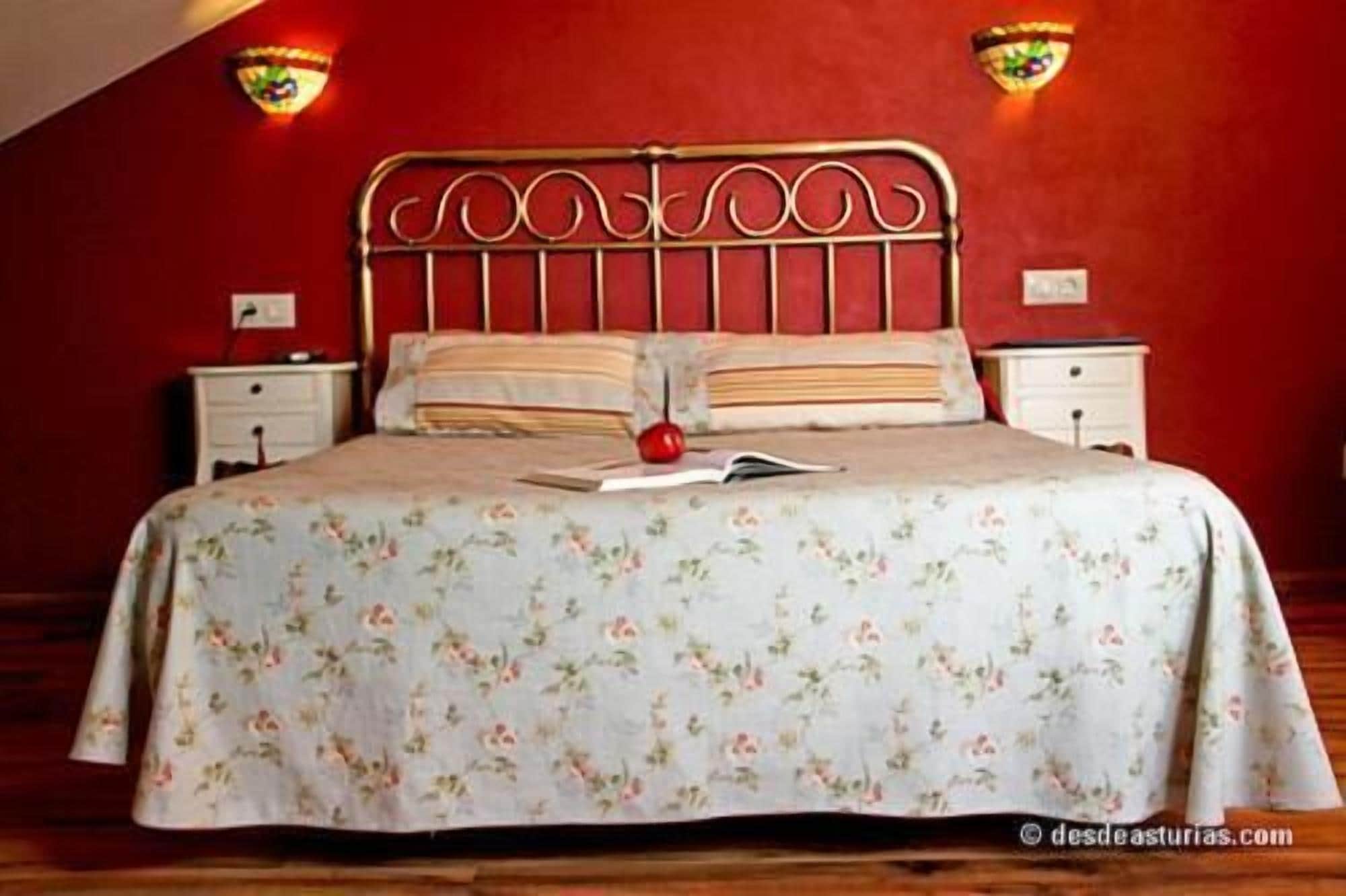 Una cama con una colcha estampada, un libro y una manzana encima. Hay dos mesitas de noche con lámparas.