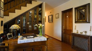 Una scala che conduce a un secondo piano, una scrivania in legno con una lampada, un vaso con fiori e quadri appesi al muro.