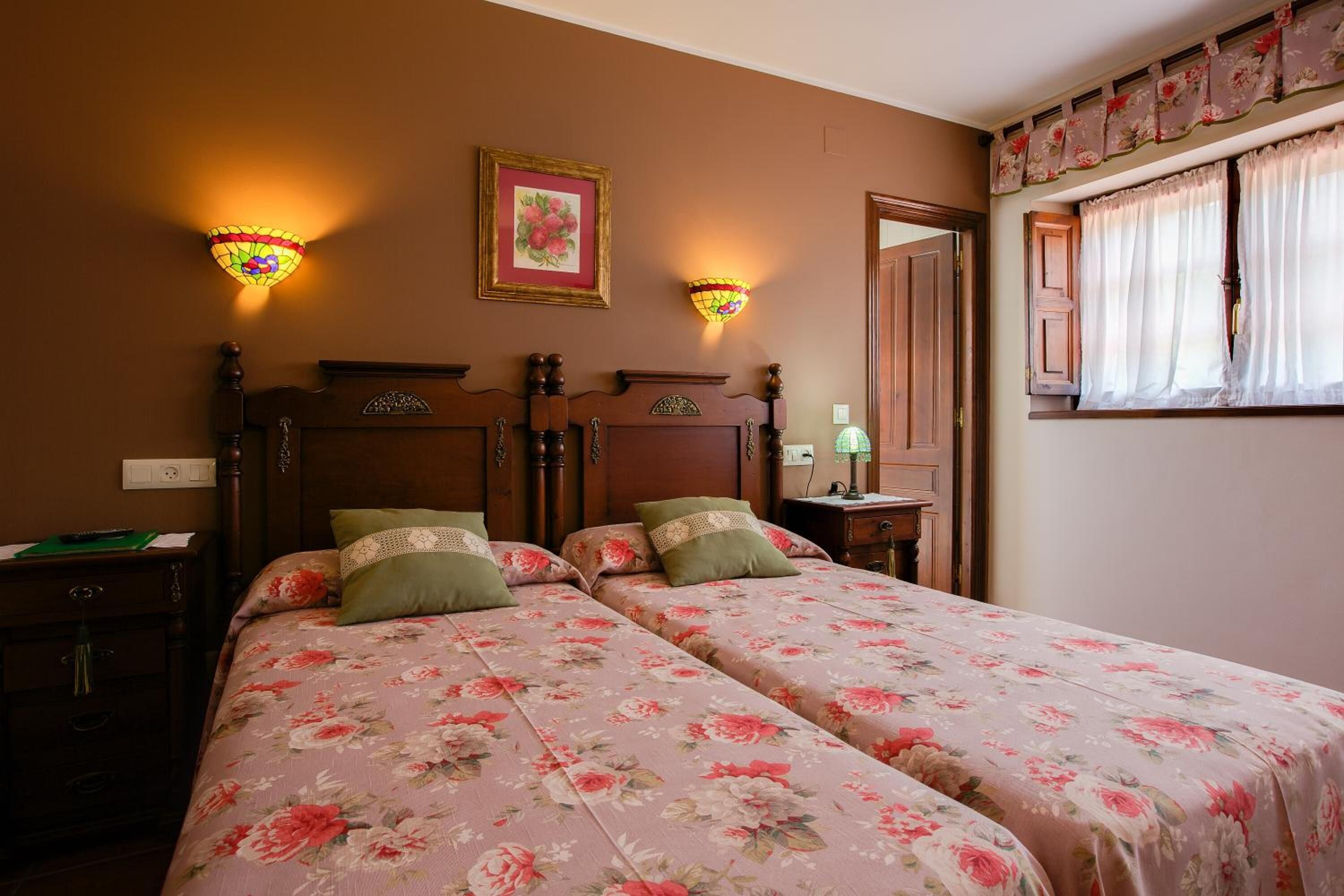 A double bed with floral bedding, a wooden headboard, two bedside tables, and wall-mounted lamps.