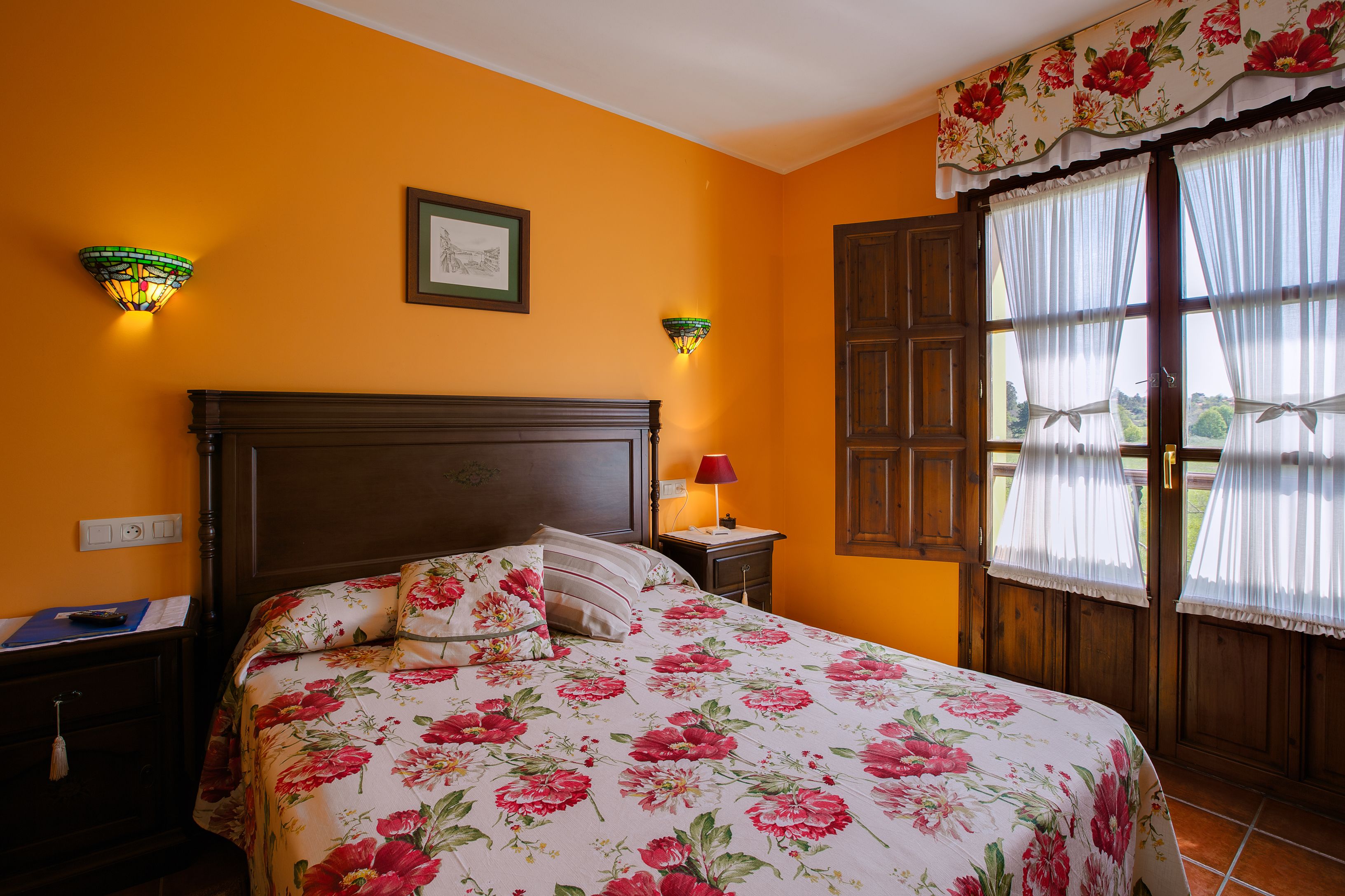 A room with a bed, a nightstand, a lamp, and a window with curtains.
