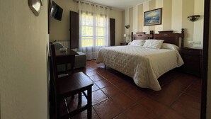 Una camera d'albergo con un letto, una scrivania, una sedia, un televisore e una finestra con tende.