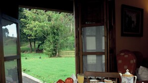 Una tavola imbandita per la colazione con pasticcini assortiti, frutta e bevande, con vista su un giardino e un recinto in legno.
