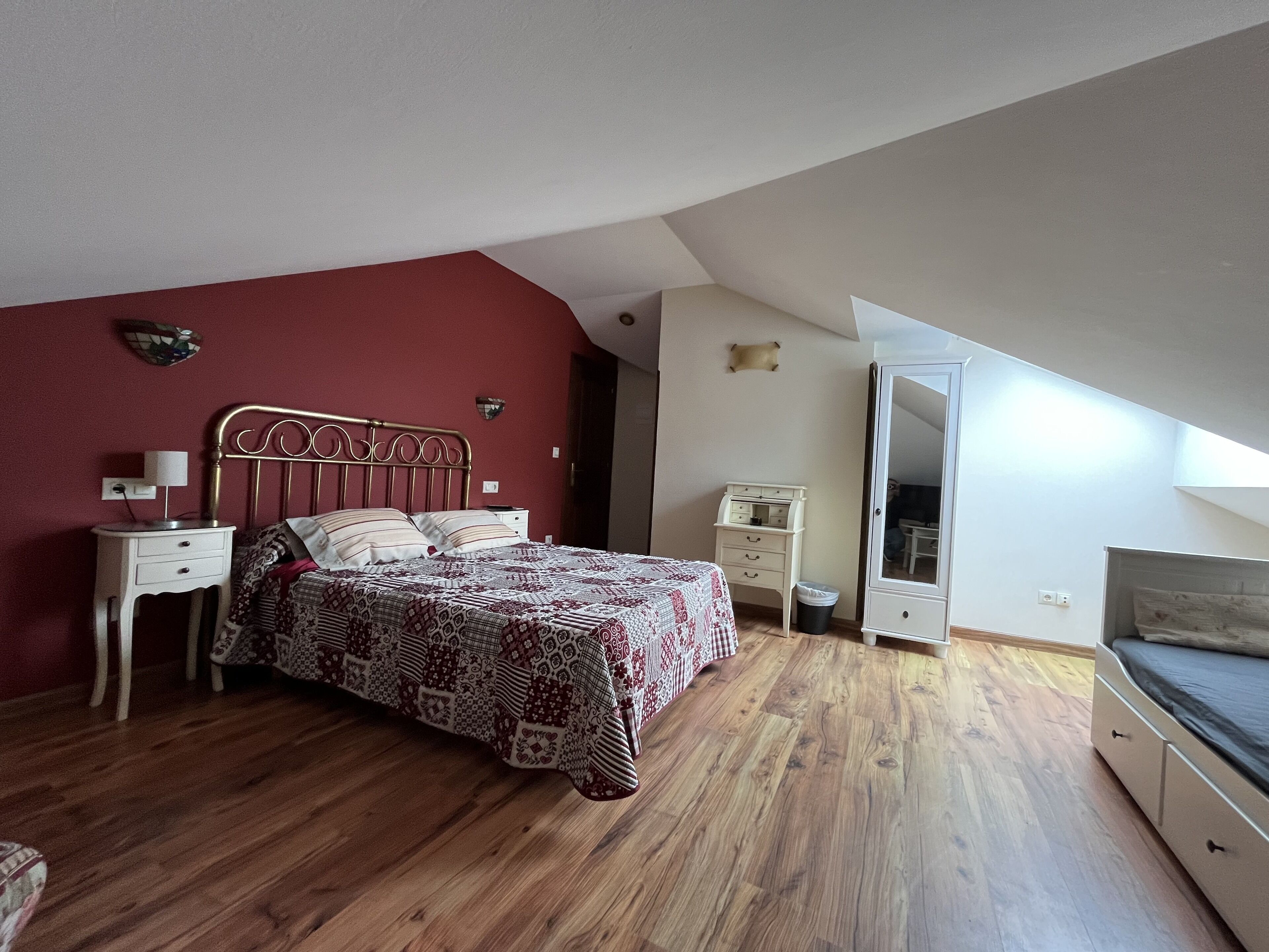 A bedroom with a wooden floor, a bed with patterned bedding, a nightstand, a dresser, and a wardrobe.