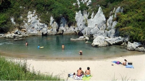 Una spiaggia con formazioni rocciose, acqua cristallina e persone che nuotano e si rilassano.
