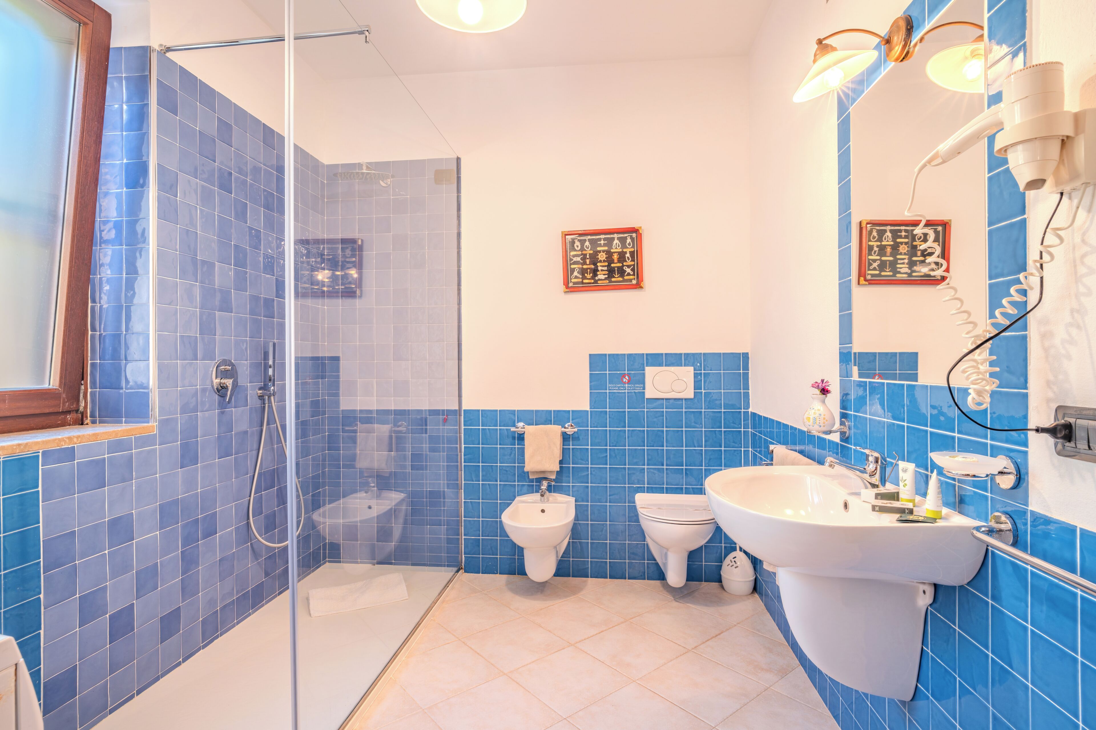 A bathroom with blue tiles, a glass shower enclosure, a sink, and two toilets.