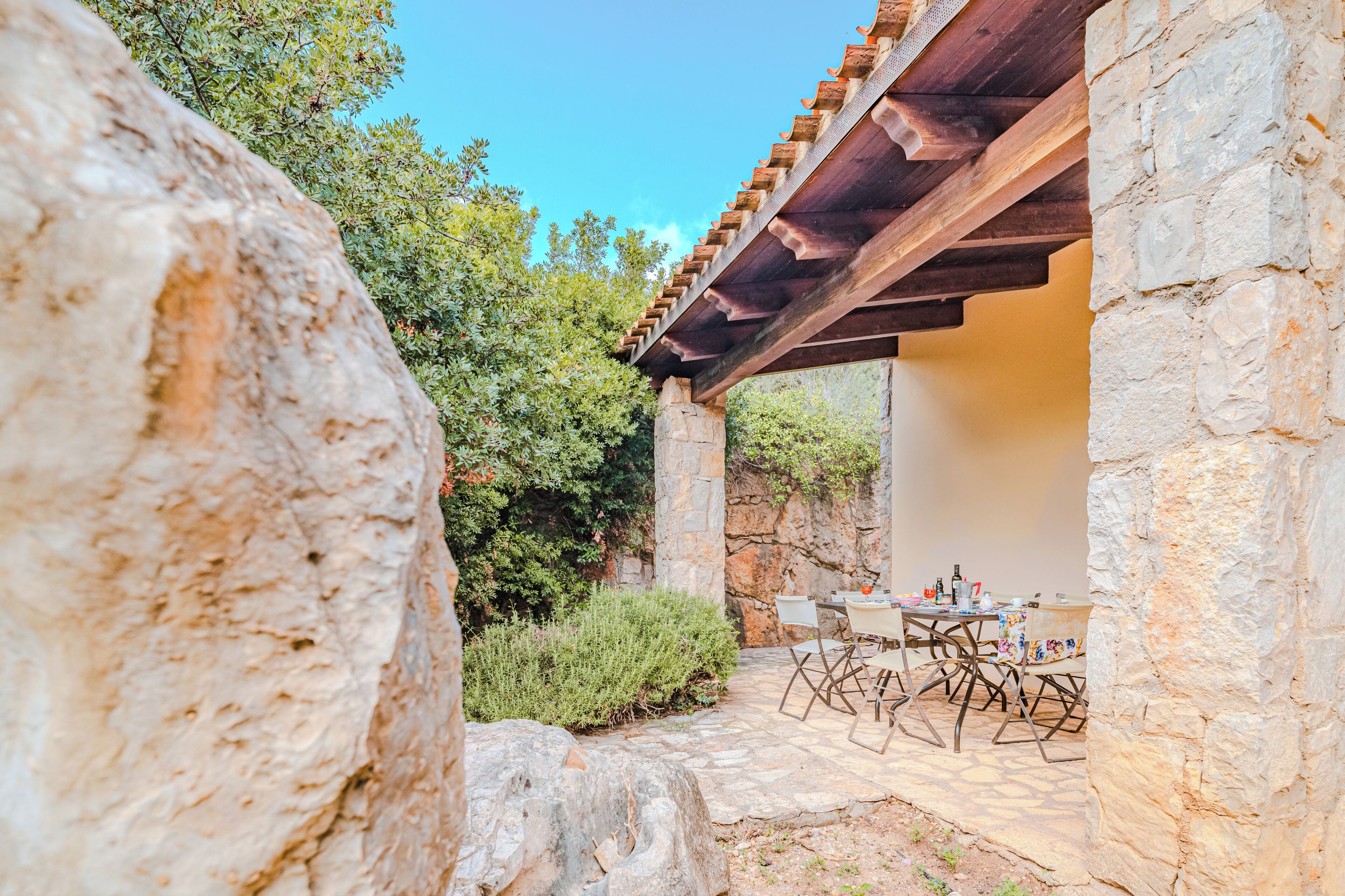 A stone building with a wooden pergola, outdoor seating, and greenery.